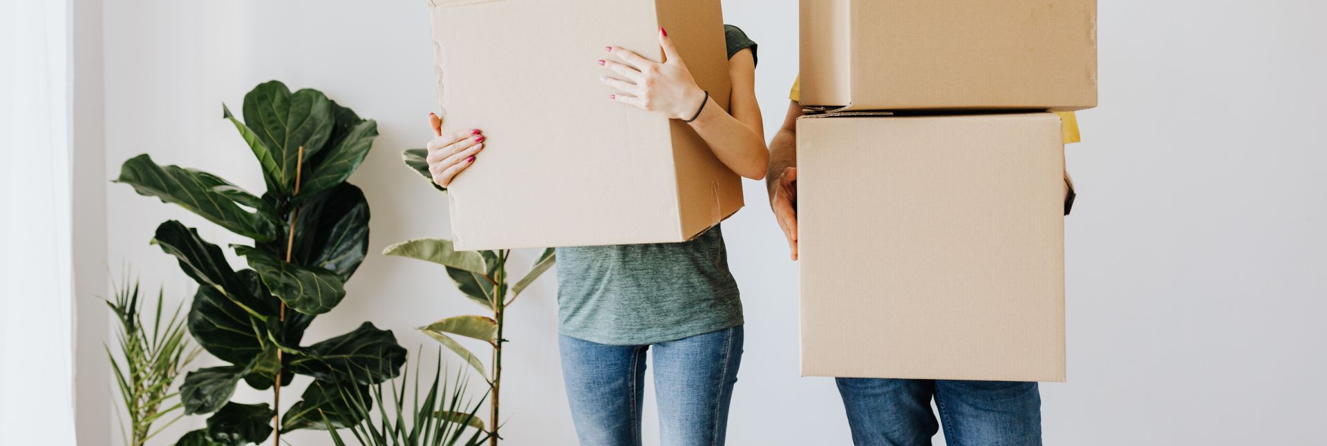 Unrecognizable couple wearing jeans standing carrying stacked carton boxes out of apartment during renovation on daytime