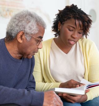 A Woman Reading a Book while Sitting Beside the Man in Blue Sweater